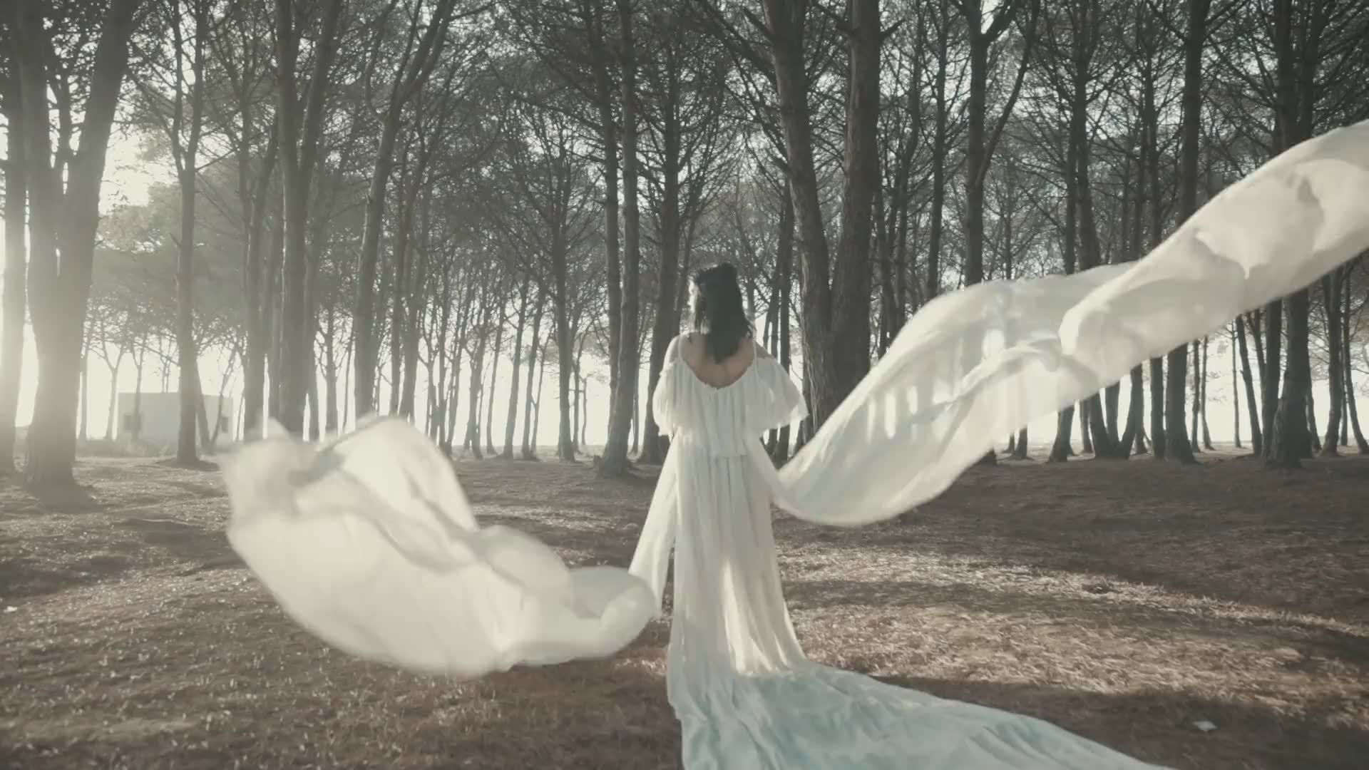 Braut im fließenden Brautkleid mit wehender Schleppe im Pinienwald – exklusive Brautmode von Cena Couture